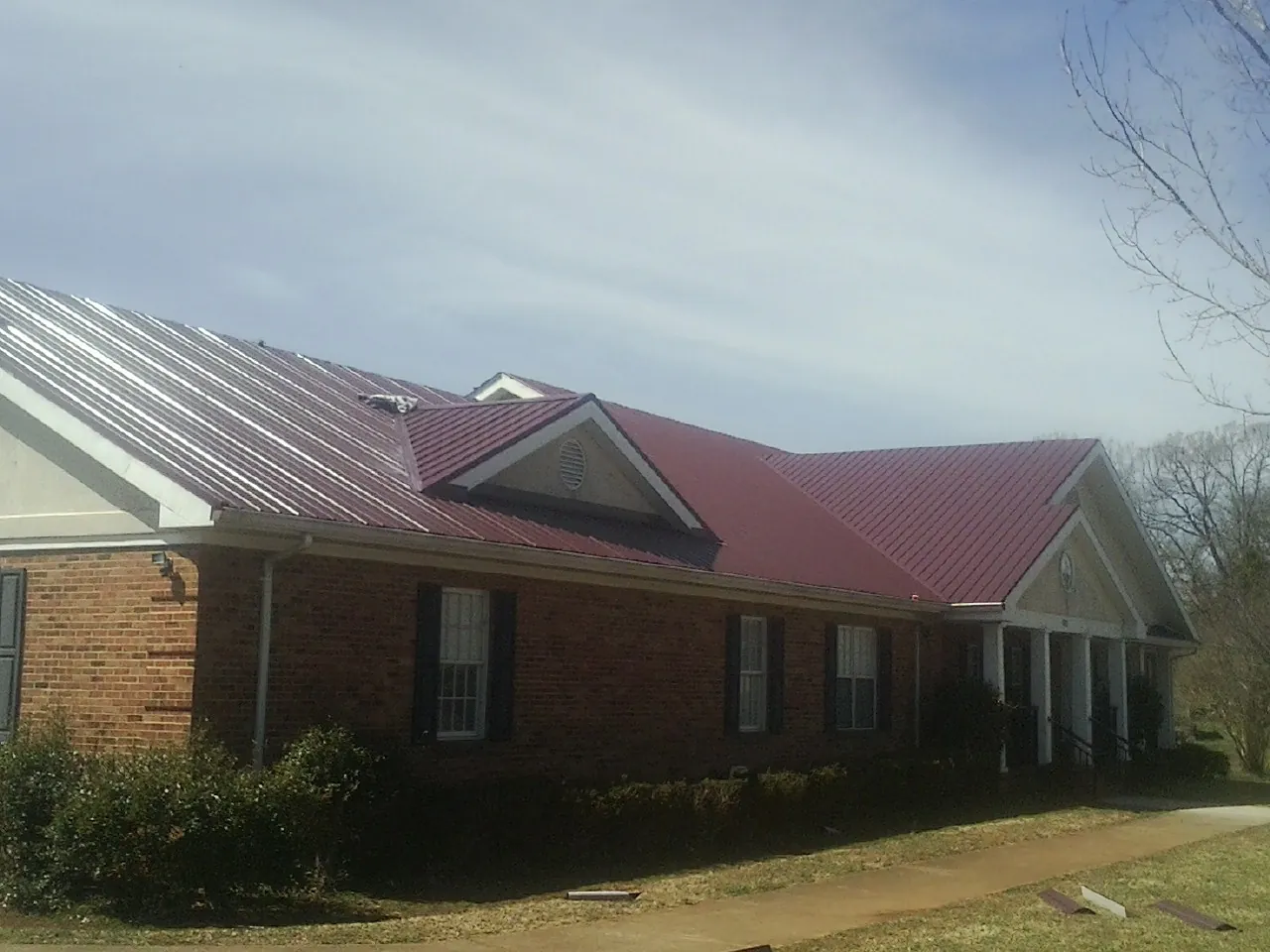 Red metal roof with gabled entries on a long brick building, from a Hail Damage Roof Repair job in Hay