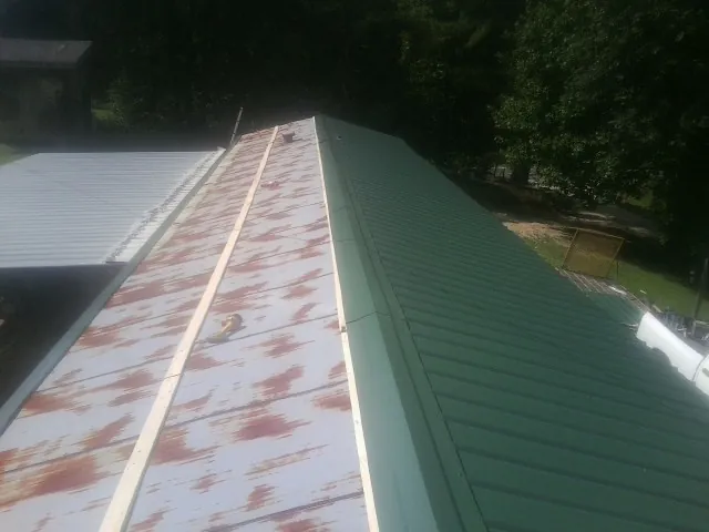 Old rusted panels beside newly installed green metal roofing — Wind Damage Roof Repair by Roofing Brothers in Hay