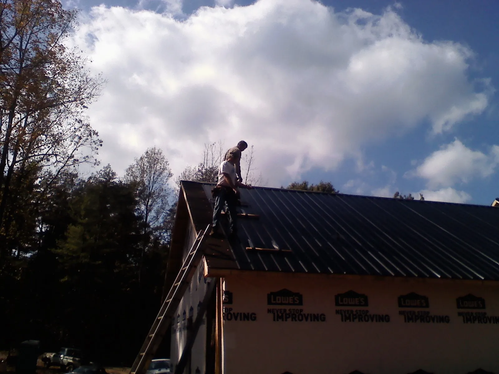 Roofer fastening dark metal panels high against a cloudy sky, from a Roof Inspection job in Hay