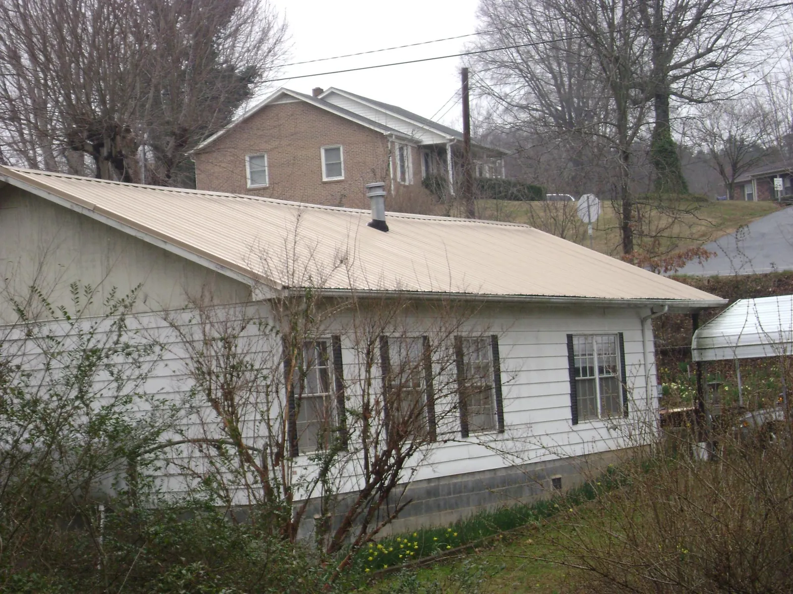 Tan metal roof on a white sided house set into a hillside — Commercial Roofing by Roofing Brothers in Hay