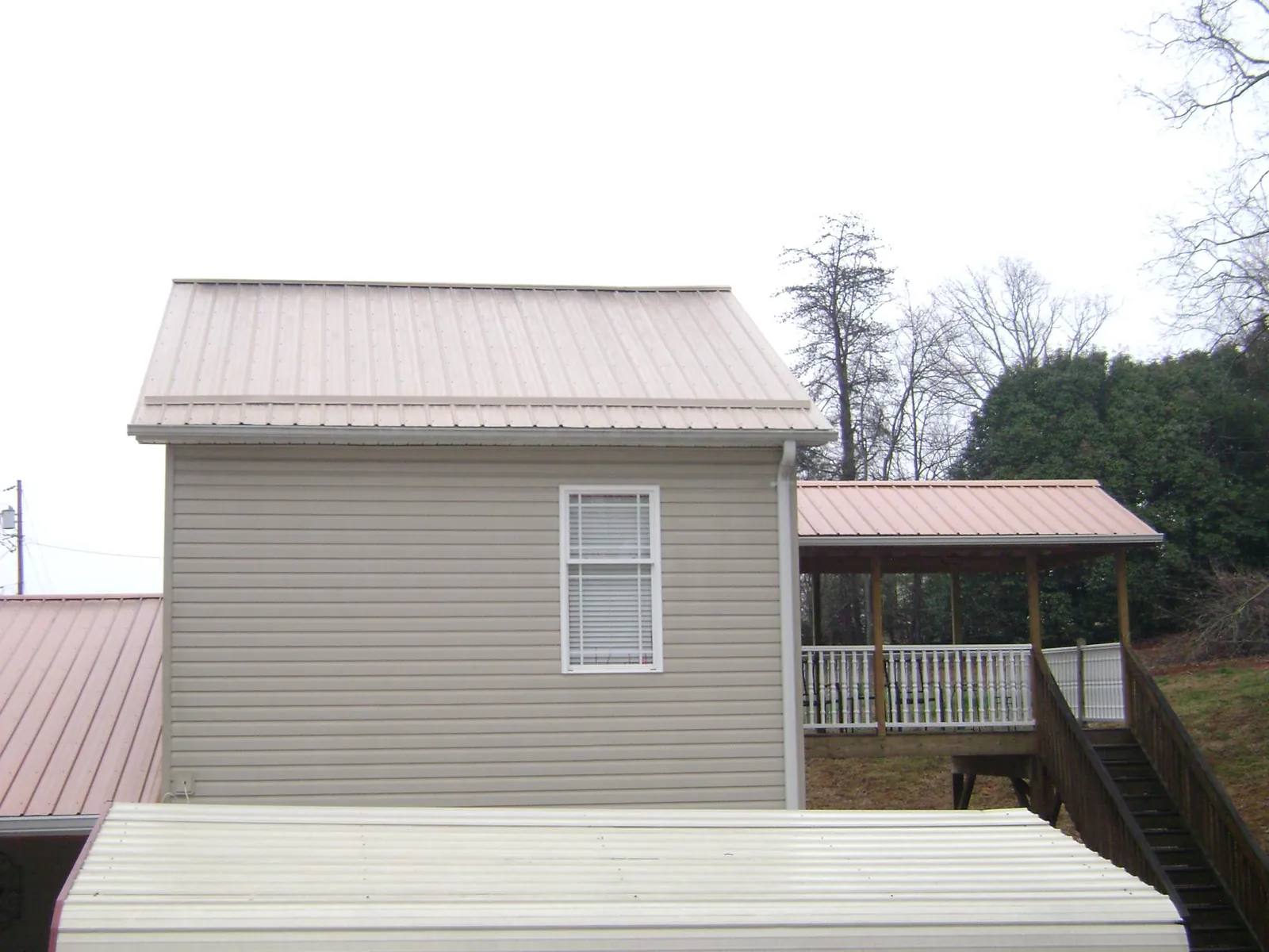 Tan metal roofs on a two story addition and attached porch, from a Roof Replacement job in Hay